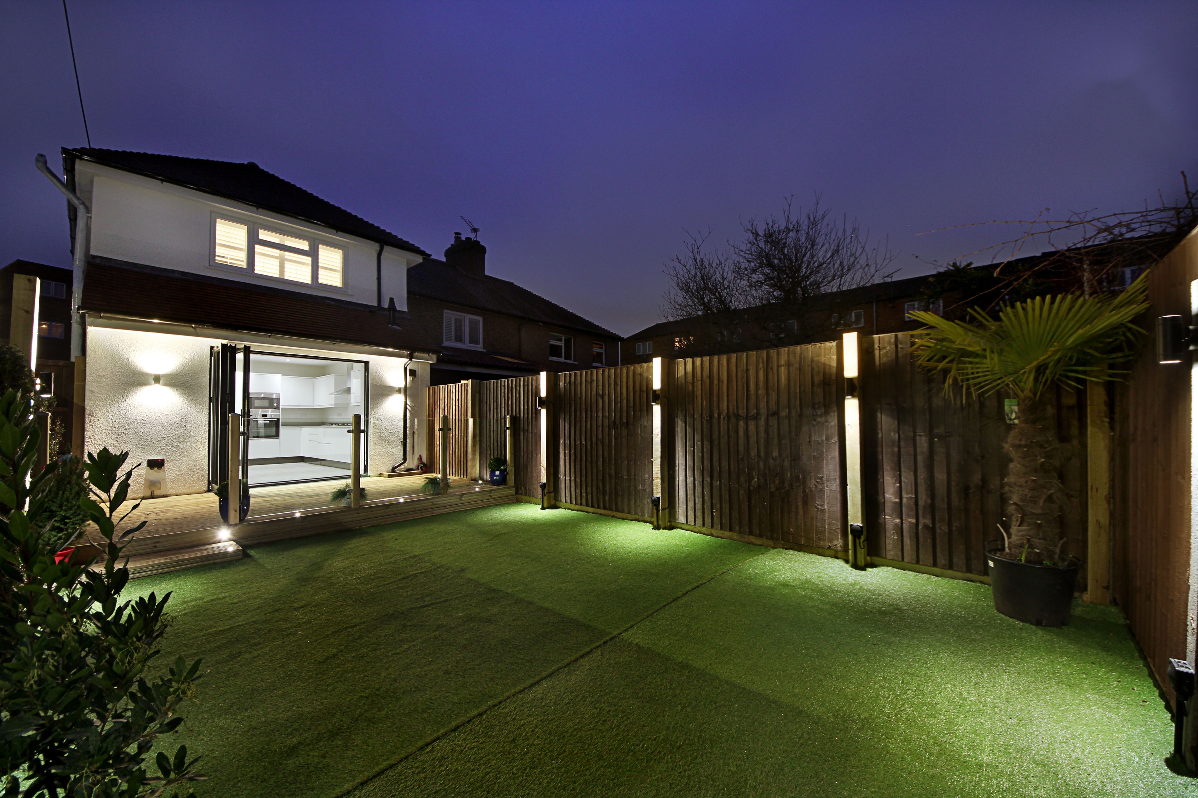 Chilton Avenue — landscaped rear garden with timber decking, glass balustrade posts and LED lighting at night