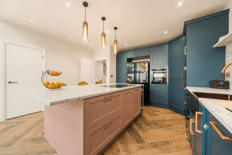 Kitchen with teal cabinetry, pink island, marble worktop and pendant lighting