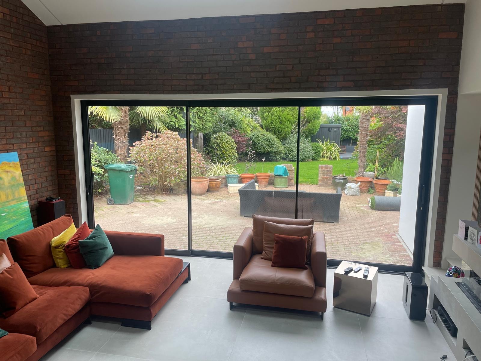 Galley Lane — double-height living room with full-width sliding glazed doors opening to garden, exposed brick walls and terracotta seating