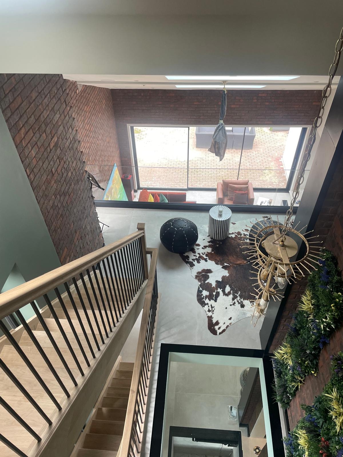 Galley Lane — overhead view from mezzanine looking down into double-height living space with living wall, glass floor void and sunburst chandelier