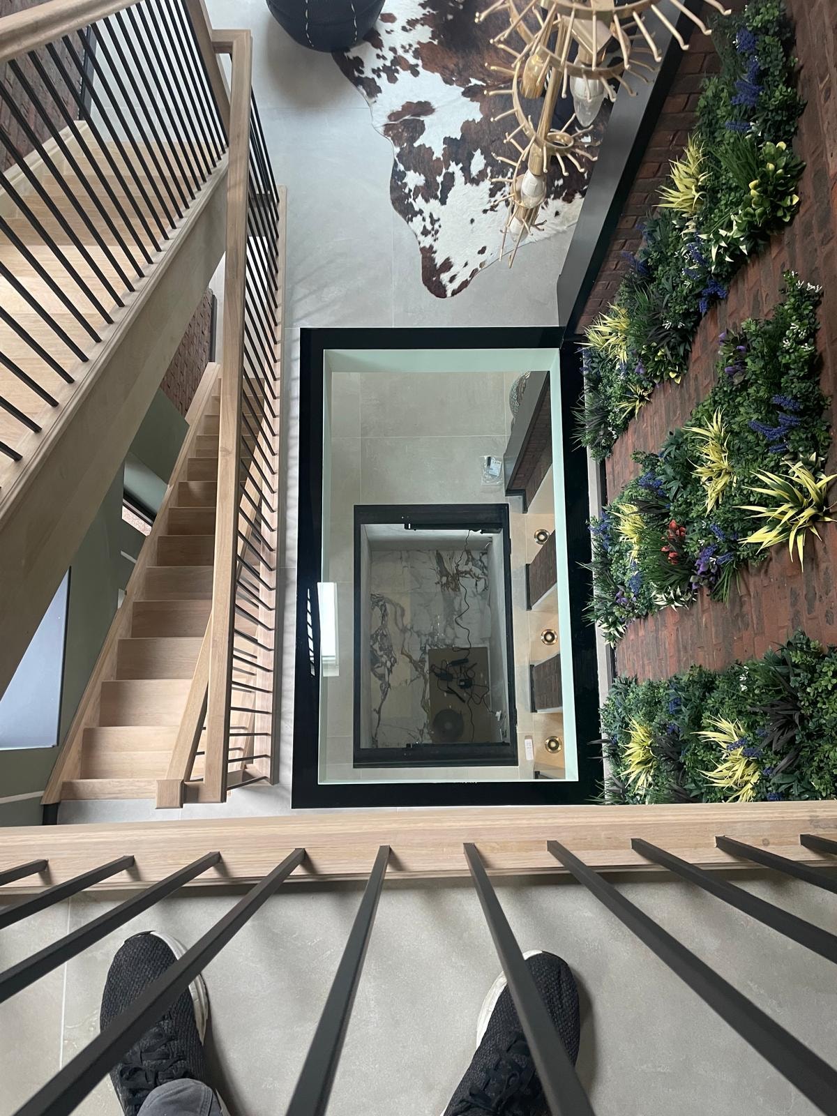 Galley Lane — overhead view down staircase into glass floor void with living wall and mezzanine landing visible