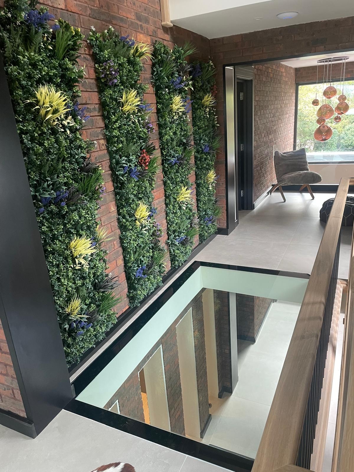 Galley Lane — full-height living wall with lush planting on exposed brick, glass floor void and mezzanine landing with copper pendants