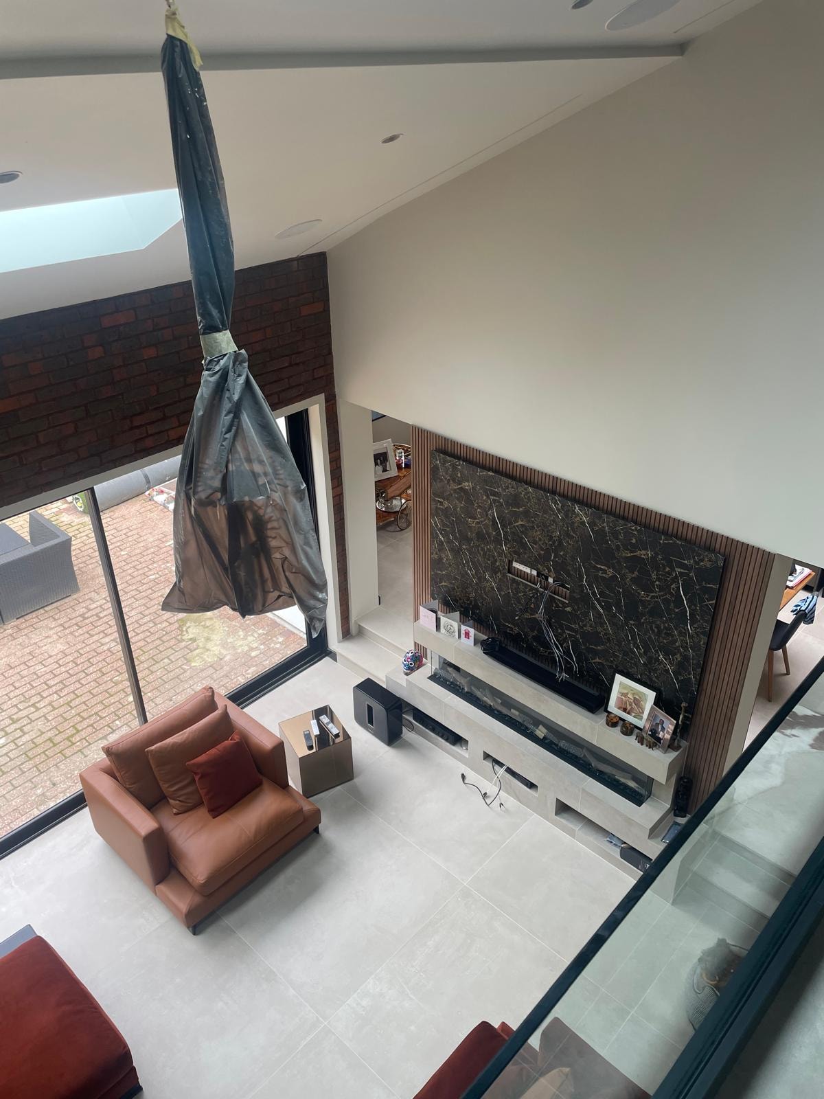 Galley Lane — overhead view from mezzanine looking down into living room showing marble TV wall, leather seating and double-height volume