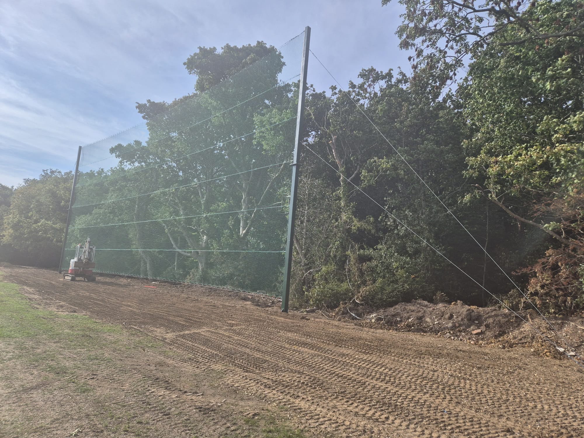 Net structure with mini excavator alongside treeline boundary