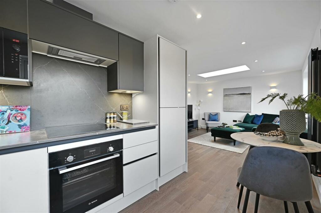Open-plan kitchen and living space with grey units, rooflight and green sofa beyond