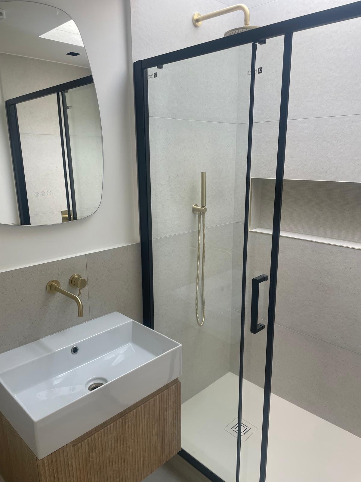 Bathroom with stone tiles, gold fittings and black-framed shower enclosure