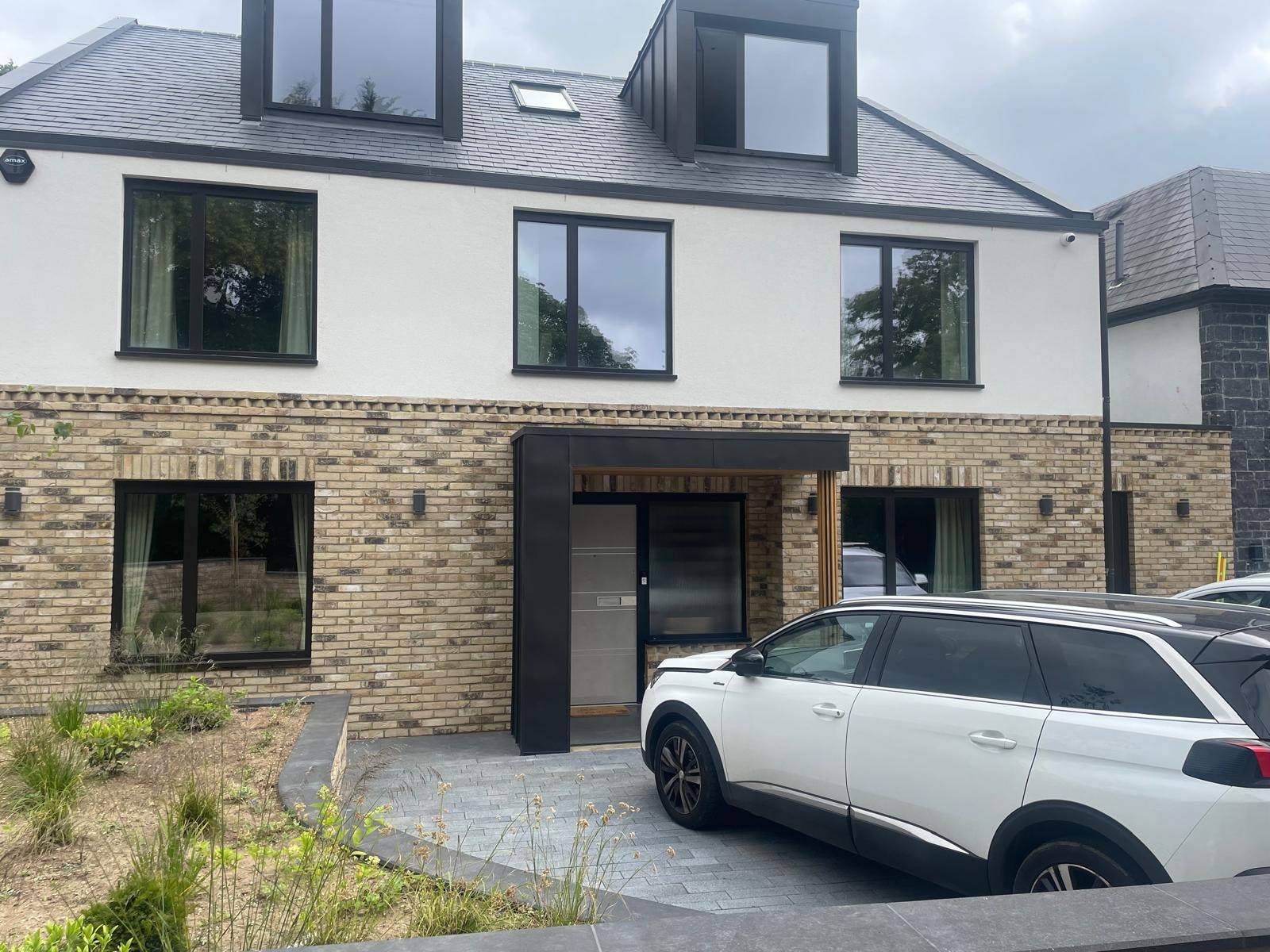 Bellfield Avenue — completed front entrance with brick plinth, white render, dark aluminium windows and timber-framed canopy